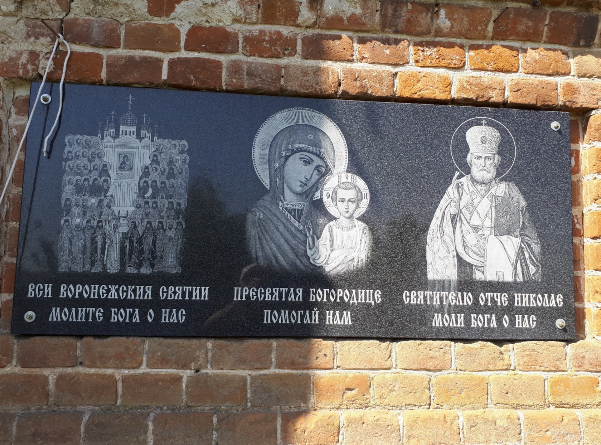 Черная гранитная мемориальная доска с изображениями святых у Казанской церкви в Октябрьском